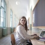 Female student typing on laptop in university hallway